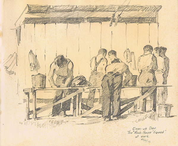 World War One Soldiers in t-shirts and suspenders washing clothes at a bench, pyramid tends in the background.