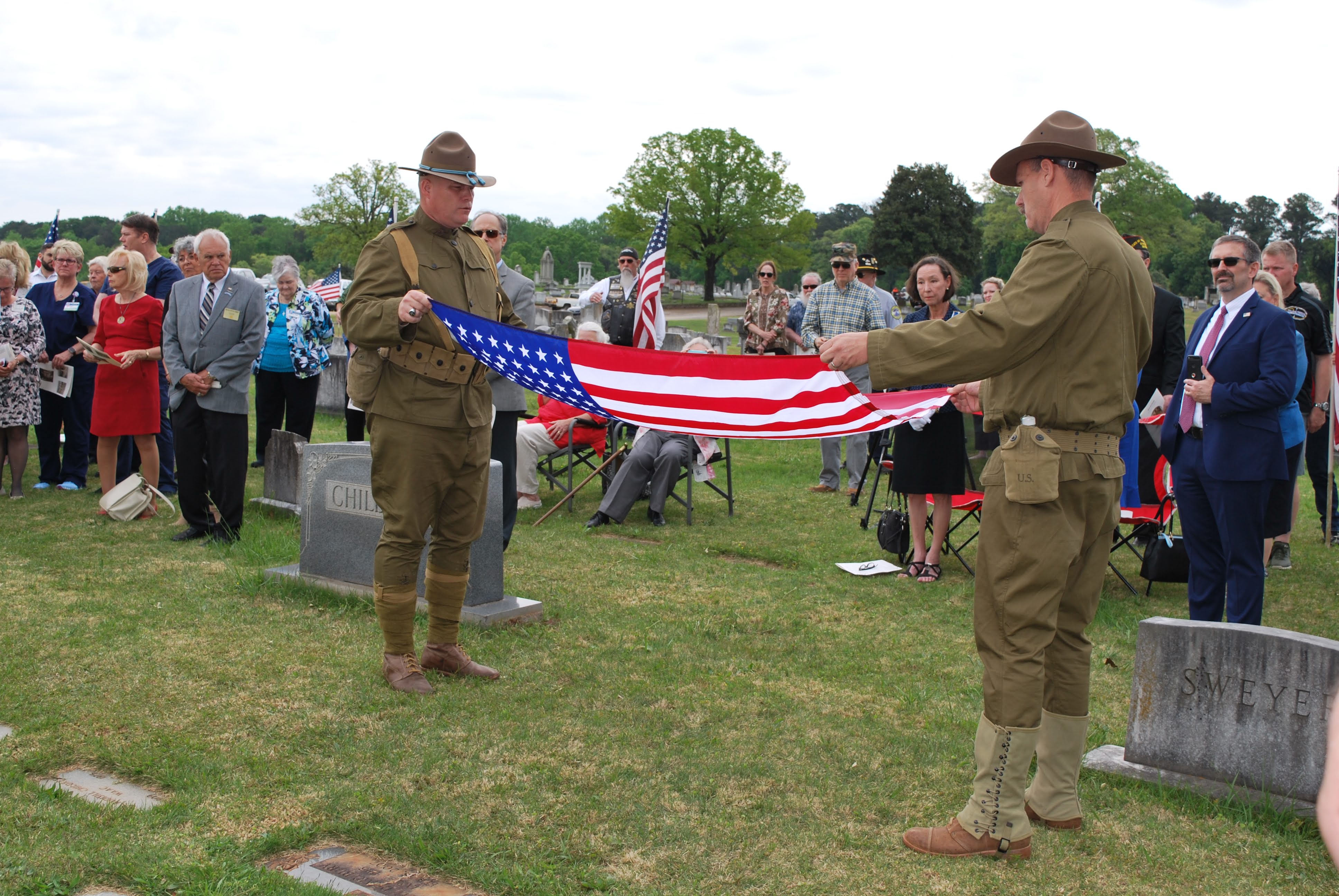 Two soldiers dressed in WW1 military uniforms folding the US flag.