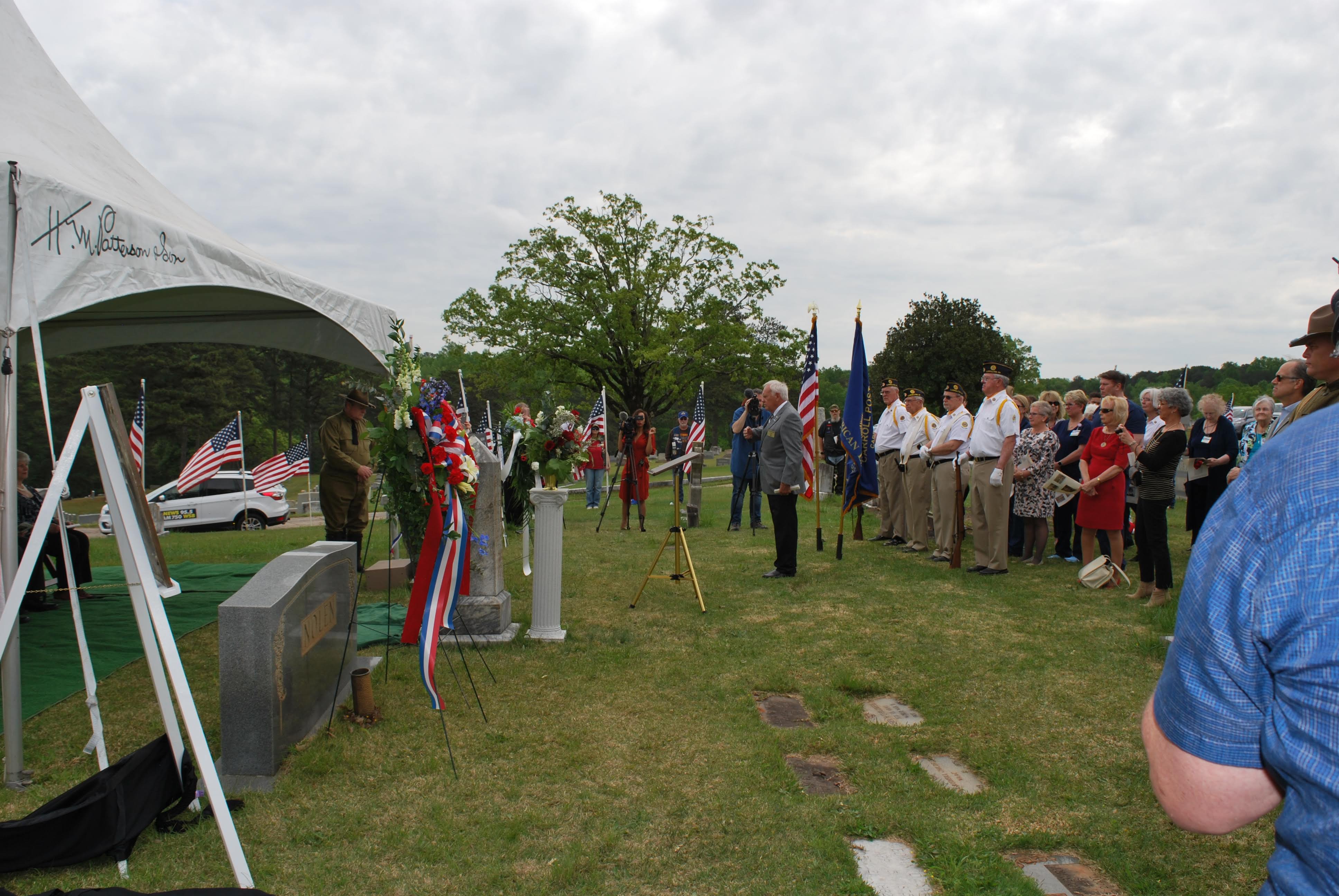 People standing around the grave marker in what looks to be a moment of silence.