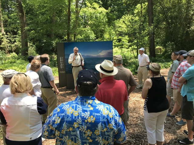 Man speaking to crowd in front of a picture of the ocean.