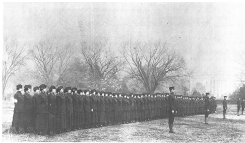 The first women of the Marine Corps Reserve stand at attention before beginning morning drill on the eclipse behind the White House, circa 1918.
