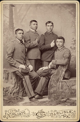 Four male students from Carlisle Indian School wearing military style uniforms, c. 1885. 